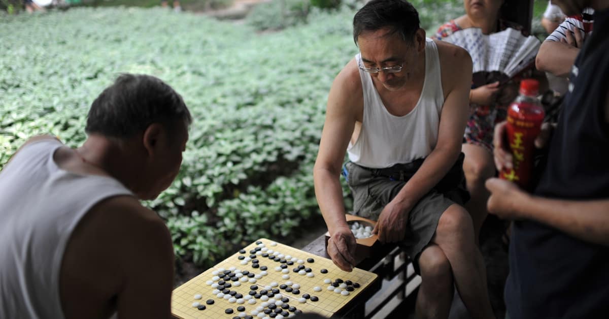 chinese park - men playing board game outdoors with spectators watching