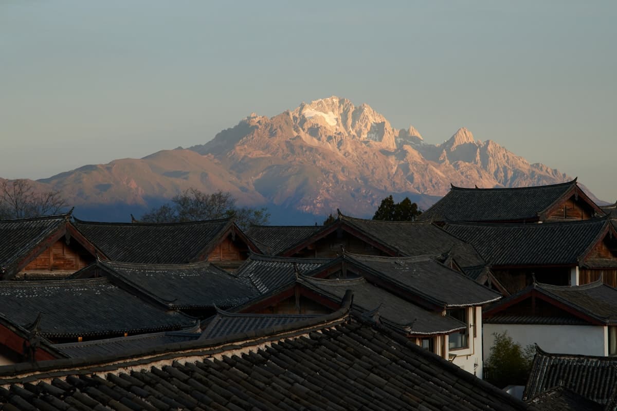 china in december - snow capped mountain peak above traditional chinese rooftops